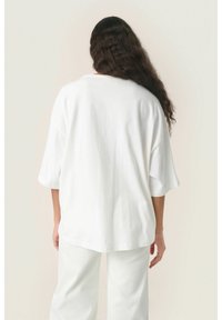 Hvid oversized kortærmet top med en afslappet pasform og rund kant, lavet af blødt materiale, parret med matchende hvide vide bukser.