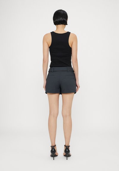 Svart ermeløs topp kombinert med grå shorts, med belted living og to baklommer. Modellen har på seg svarte høyhælte sandaler.