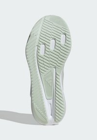 De buitenzool van de schoen is voorzien van een gestructureerde groene rubberen onderkant met een patroon voor grip, benadrukt door een witte tussenzool en branding met de tekst "ADIWEAR."
