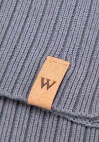 Bonnet tricoté gris avec texture côtelée, doté d'une étiquette en cuir beige avec un logo "W" embossé. Le design comprend un bord roulé.