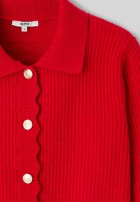 Cardigan rouge en tricot avec un col à revers, présentant une texture côtelée et une patte de boutonnage festonnée, ornée de boutons dorés.
