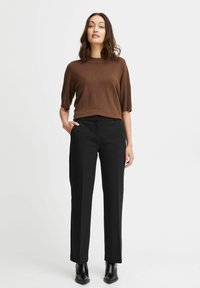 Brązowy top z krótkim rękawem w połączeniu z czarnymi, dopasowanymi spodniami, o luźnym kroju i gładkiej fakturze. Całość dopełniają czarne botki za kostkę.