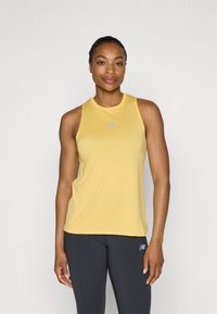 Mouwloos geel sporttanktop met een gladde textuur en lichte stof. Bevat een klein blauw logo op de borst. Gekocht met een donkere legging.