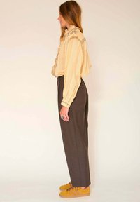 Blouse rayée jaune avec un col à volants, accompagnée d'un pantalon taille haute marron foncé et de baskets en daim jaunes avec des accents marron.