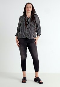 Black and white striped button-up shirt, black skinny jeans, and black heeled sandals. Smooth texture and tailored fit are visible.
