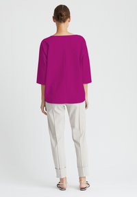 Magenta-Bluse mit Bootsausschnitt und Dreiviertelärmeln, kombiniert mit cremefarbenen, knöchellangen Hosen mit umgeschlagenen Säumen und hellen Schuhen.