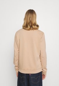 Felpa beige con scollo rotondo, polsini e orlo a costine. La vista posteriore mostra una texture del tessuto liscia e dettagli di cucitura minimi.