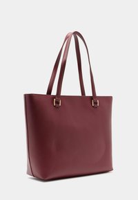 Ruda veiklos maišas su lygiu paviršiumi, dviem ilgais rankenomis ir auksinės spalvos detalėmis. Pasižymi struktūrizuota forma ir minimalistiniu dizainu.