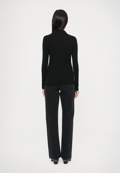 Schwarzes Langarmoberteil mit Kragen kombiniert mit schwarzen Jeans mit weitem Bein, die eine glatte Textur und einfaches Design zeigen.