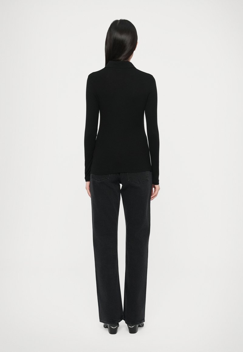 Zwart top met lange mouwen en een kraag, gecombineerd met zwarte jeans met wijde pijpen, met een gladde textuur en eenvoudig ontwerp.