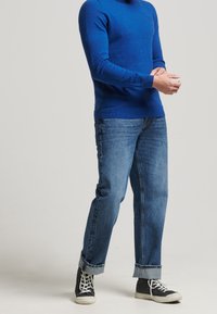 Pull en maille bleu à manches longues, associé à un jean en denim bleu clair. Comprend des manches retroussées et des baskets montantes noires.