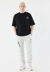 Zwarte T-shirt met korte mouwen en logo, gecombineerd met lichtgrijze cargobroek met zijritsen en witte sneakers. Minimalistisch ontwerp.