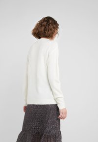 Witte, zachte trui met lange mouwen, geribbelde boorden en zoom. Draagt over een donkere, gebloemde rok, met een ontspannen pasvorm en een minimalistisch ontwerp.