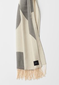 Sjaal van een wolmix met een crèmekleurige basis en grijze geometrische patronen, afgewerkt met franjes aan de uiteinden en een klein zwart label.