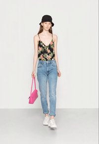 Top camiseiro preto com padrões florais e alças finas, jeans de cintura alta azul clara, sapatilhas brancas e uma bolsa rosa. O modelo usa um chapéu de balde preto.