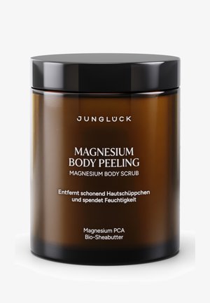 Amber glass jar with a black lid. White text displays product name: "Magnesium Body Peeling" and additional details in German.