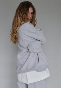 Szary sweter z luźnym krojem i oversize'owymi rękawami, nałożony na białą koszulę, wykonany z miękkiego materiału i z detalicznym przeszyciem.