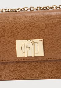 Brun læderhåndtaske med en tekstureret finish, der har en guldfarvet metalspænde og kæderem. Designet er slankt med minimalistiske detaljer.