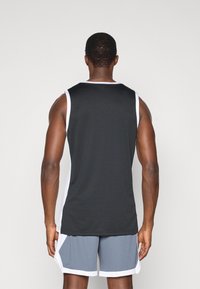 Zwarte sport tanktop met witte zijaccenten, met een gladde textuur en zonder mouwen, gecombineerd met lichtgrijze shorts.