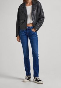 Svart läderbikerjacka, vit kort topp, blå denimjeans och svarta och vita sneakers. Släta texturer och figursydd design.