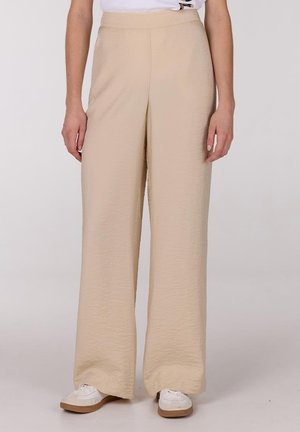 Beige wijde broek met een gestructureerd oppervlak, een hoge taille en een vloeiende ontwerp. Gecombineerd met witte sneakers en een eenvoudig shirt.