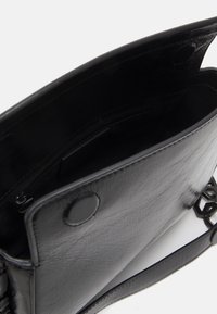 Czarna skórzana torba na ramię otwarta, ukazująca wnętrze z kieszonką na zamek błyskawiczny i zapięciem na magnes na białym tle.