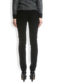 Pantalons noirs ajustés avec une texture lisse, présentant une taille mi-haute et une conception de jambe fuselée. Portés avec des chaussures à talons hauts.
