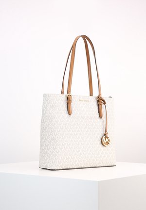 Hvid Michael Kors tote-taske med beige læderhåndtag og gyldent logohæng, der vises på en hvid piedestal.