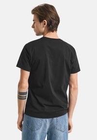 Sort bomulds T-shirt, rund hals, korte ærmer, afslappet pasform, ensfarvet design, ingen synlige prints. Båret med lyseblå denim jeans.