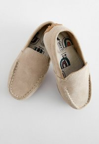 Chaussures slip-on en daim beige avec un accent cousu, bout rond et semelle intérieure à motifs comportant des éléments colorés. Semelle en caoutchouc.