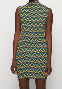 Ärmelloses Kleid mit einem Zickzackmuster in Lila, Grün, Gelb und Blau. Hoher Ausschnitt mit taillierter Silhouette und kurzer Länge.