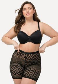 Zwarte bh heeft voorgevormde cups met een decoratieve strik, gecombineerd met sheer zwarte shorts die een zigzagpatroon en een elastische tailleband hebben.