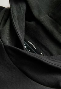 Top de tela negra con cuello doblado, que presenta una textura suave. La etiqueta dice "ALLSAINTS" y está situada en el escote.