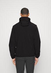 Chaqueta negra ligera con cuello alto y puños elásticos, que presenta un corte holgado y una tela suave y resistente al agua.