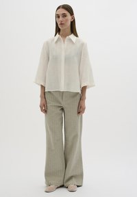 Blusa blanca texturizada con un cuello tipo camisa, combinada con pantalones de pierna ancha verde claro con patrones verticales y zapatos planos beige.