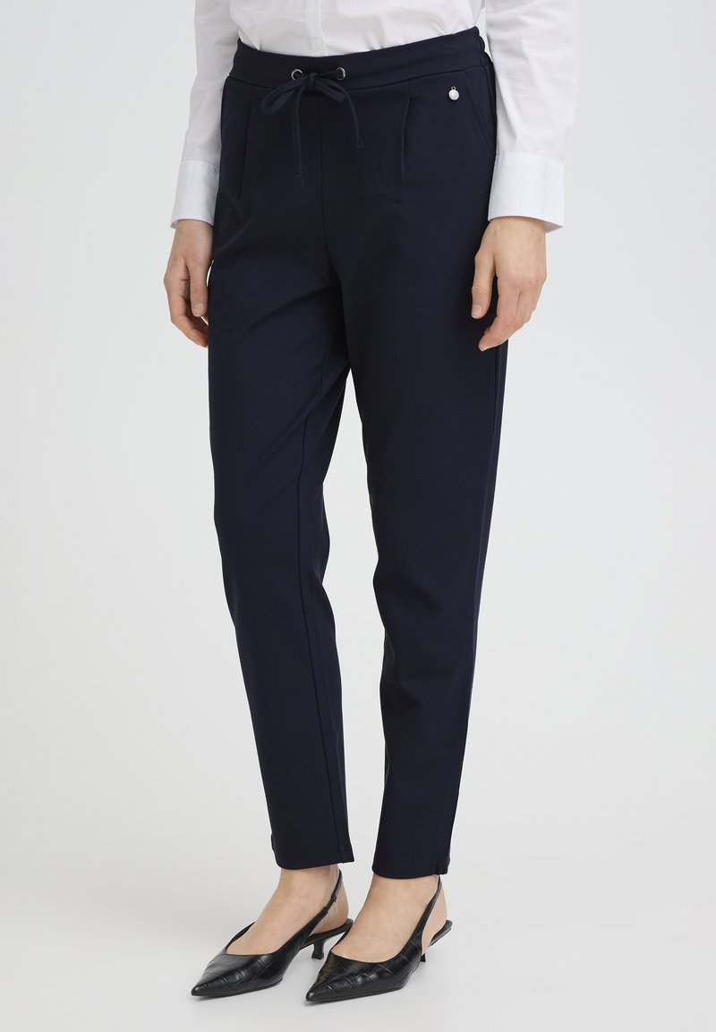 Pantaloni bleumarin cu talie ajustabilă prin șnur, buzunare laterale și detaliu metalic. Material neted, design slim fit și tiv la nivelul gleznei.