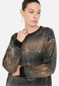 Maglione con paillettes con un gradiente orizzontale che va dal marrone al nero, dotato di polsini a coste e scollatura rotonda. Il modello mostra una mano appoggiata sul braccio.