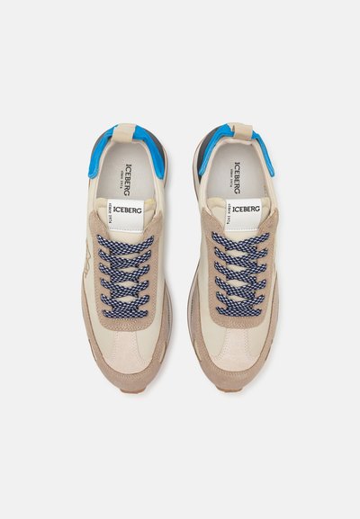 Beżowe sneakersy z niebieskimi akcentami i granatowymi sznurowadłami. Wykonane z zamszu i skóry, z okrągłym noskiem oraz teksturowaną podeszwą. Logo na pięcie.