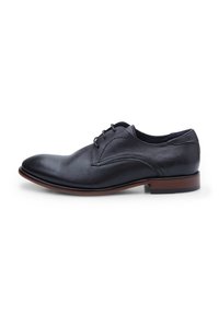 Scarpa da uomo in pelle nera forata, con punta rotonda, sistema di allacciatura e suola in tono legno contrastante. Tessitura liscia complessivamente.