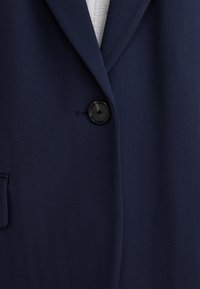 Námořnický modrý blazer s herringbone vzorem, na jedno černé knoflíkové zapínání a boční kapsou. Hladká textura s přizpůsobeným střihem.