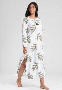Maxiklänning i vitt med grönt ormbunksmönster, långa ärmar, sidoklämmor och en knytning i halsen. Tillverkad av lätt, texturerad tyg.