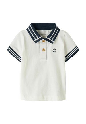 Biała koszulka polo z krótkim rękawem dla małych dzieci, z granatowym paskowanym kołnierzykiem i mankietami, dwoma brązowymi guzikami i małym granatowym emblematem kotwicy na piersi.