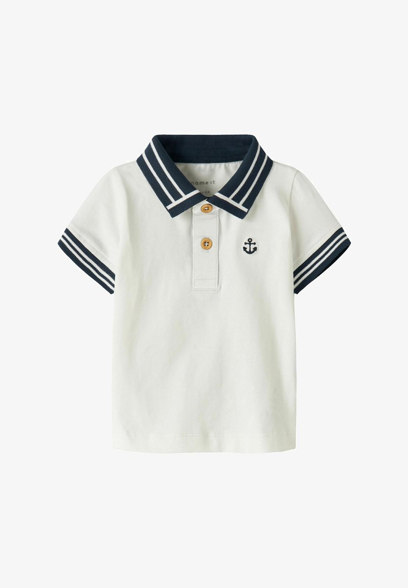Λευκό κοντομάνικο πόλο για νήπια με κολάρο και μανσέτες ριγωτές σε ναυτικό μπλε, δύο καφέ κουμπιά και μικρό ναυτικό μπλε έμβλημα άγκυρας στο στήθος.