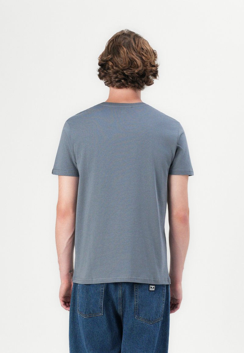 Graues Rundhals-T-Shirt aus Baumwolle mit kurzen Ärmeln und lockerer Passform. Auf der Rückseite befindet sich ein kleines Markenetikett nahe dem Saum.