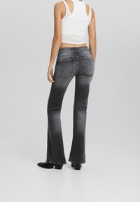 Jeans de campana en gris oscuro con una cintura de altura media, dos bolsillos traseros y un ligero desgaste. Tejido de mezcla de algodón con una textura suave.