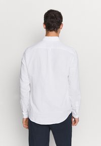 Camicia bianca a maniche lunghe realizzata in un tessuto leggero, con colletto classico, polsini con bottoni e orlo curvo sul retro.