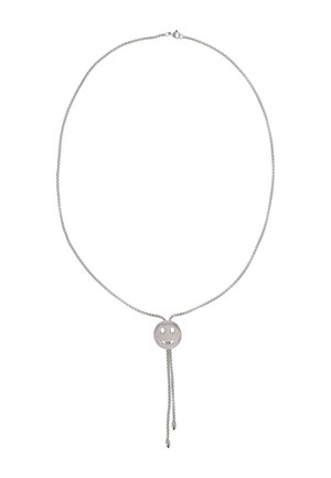 Hopeinen ketjukaulakoru, jossa säädettävä liukusäädin, kiillotettu hymyilevä kasvokuvio ja kaksi roikkuvaa ketjun päätä.