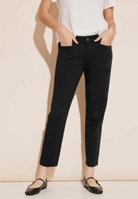 Jeans neri slim-fit con vita media, dotati di tasche frontali e una texture liscia, abbinati a un top bianco con texture e mocassini neri.