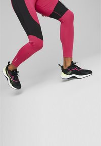 Czarne buty sportowe z różowymi akcentami i fakturowaną cholewką, zestawione z dopasowanymi różowo-czarnymi legginsami z dynamicznymi panelami.