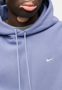 Ανοιχτό μοβ φούτερ με κουκούλα από μαλακό ύφασμα, με λευκό λογότυπο Nike και κορδόνια, σε άνετη γραμμή και με διακριτική υφή.
